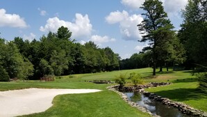 Ein Golfplatz mit einem Sandbunker, einem Teich und einer Holzbrücke.