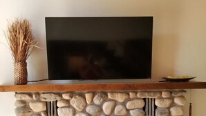 Ein Kamin aus Stein mit einem Flachbildfernseher darüber, ein gewebter Korb links und ein Holzregal mit Obst rechts.