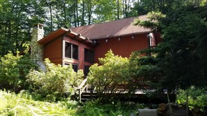 Ein rustikales Blockhaus mit Steinkamin, umgeben von dichtem Grün und Bäumen.