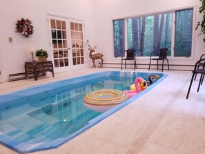 Piscina interna com vista para uma floresta através de grandes janelas.