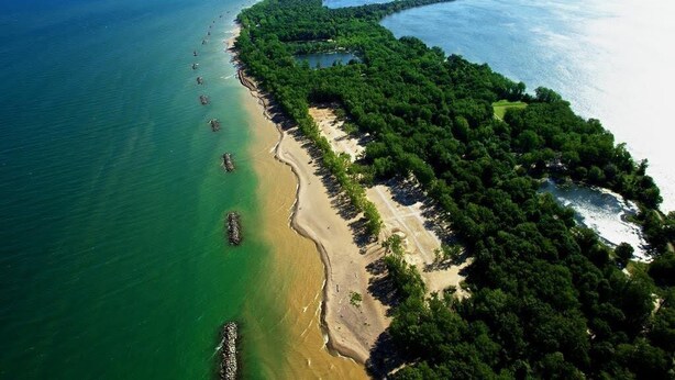 An aerial view of a coastal area with a long stretch of beach, dense forest, and clear blue waters.