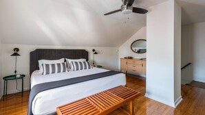 A bedroom with a bed, a ceiling fan, a wooden bench, a dresser, and a mirror.