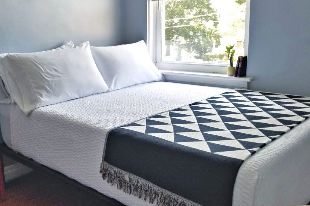 Un letto rifatto con cura, con biancheria bianca e una coperta a motivi geometrici.
