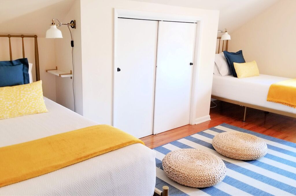 Un dormitorio con cama, mesita de noche, lámpara, armario y un sofá con cojines.