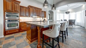A modern kitchen with wooden cabinets, stainless steel appliances, and a large island with bar stools. - Serene Scottsdale Home:Heated Pool,HotTub,FirePit,Putting Green & Mountain Views (Scottsdale)