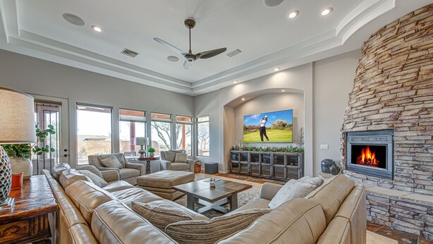 A spacious living room with a stone fireplace, leather sofas, and a flat-screen TV displaying golf. - Serene Scottsdale Home:Heated Pool,HotTub,FirePit,Putting Green & Mountain Views (Scottsdale)