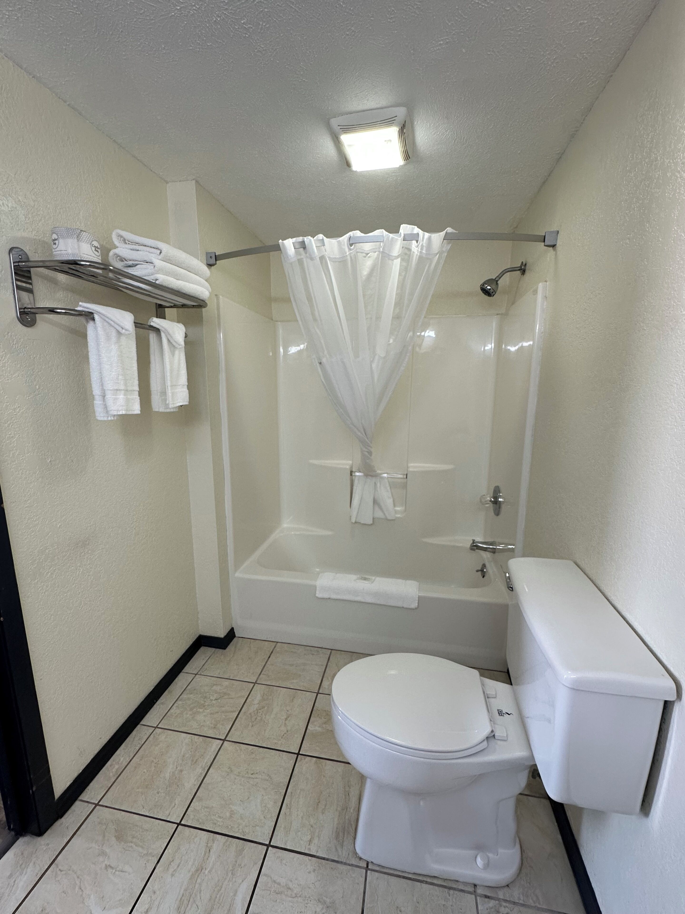 A bathroom with a toilet, a bathtub with a shower curtain, and a towel rack with folded towels.