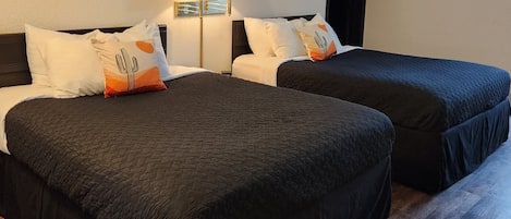 A hotel room with two beds, dark bedding, and artwork on the walls.