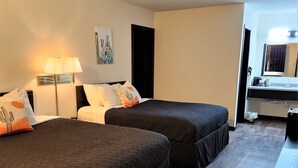 A hotel room with two beds, a desk, a bathroom, and a painting on the wall.