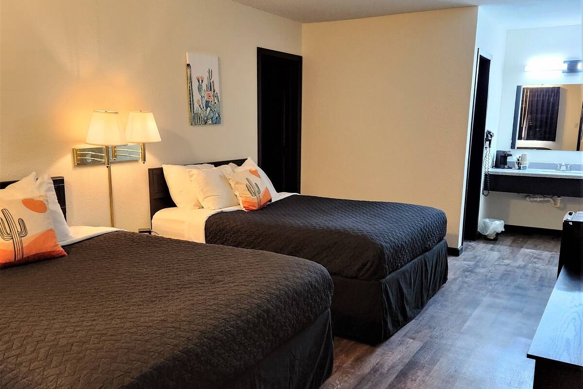Ett hotellrum med två sängar, ett skrivbord, ett badrum och en tavla på väggen.