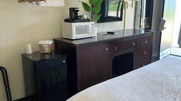 A hotel room with a bed, a desk with a microwave, a coffee maker, a plant, and a TV.