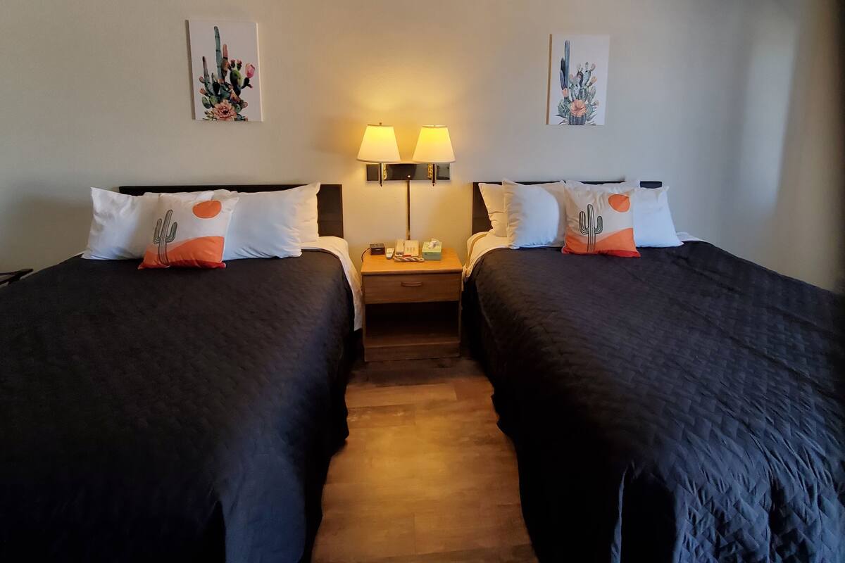 Ett hotellrum med två sängar, båda med mörkt sänglinne och kuddar med ett kakustema. Det finns två sänglampor och ett nattduksbord med en telefon och en näsdukask. Rummet har ett trägolv och vita väggar med kakusmotiv på taket.