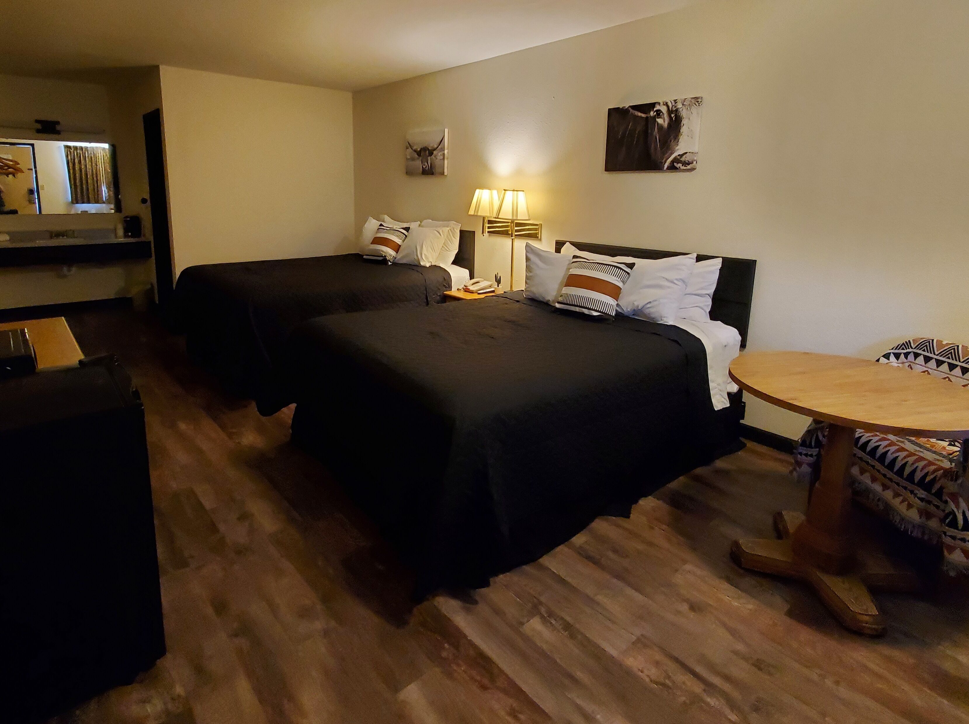 Ett hotellrum med två sängar, ett trägolv, ett runt träbord och en lampa.