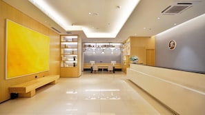 Área de recepção de hotel com design moderno, incluindo balcão de atendimento, espaço de estar e uma grande obra de arte amarela na parede.