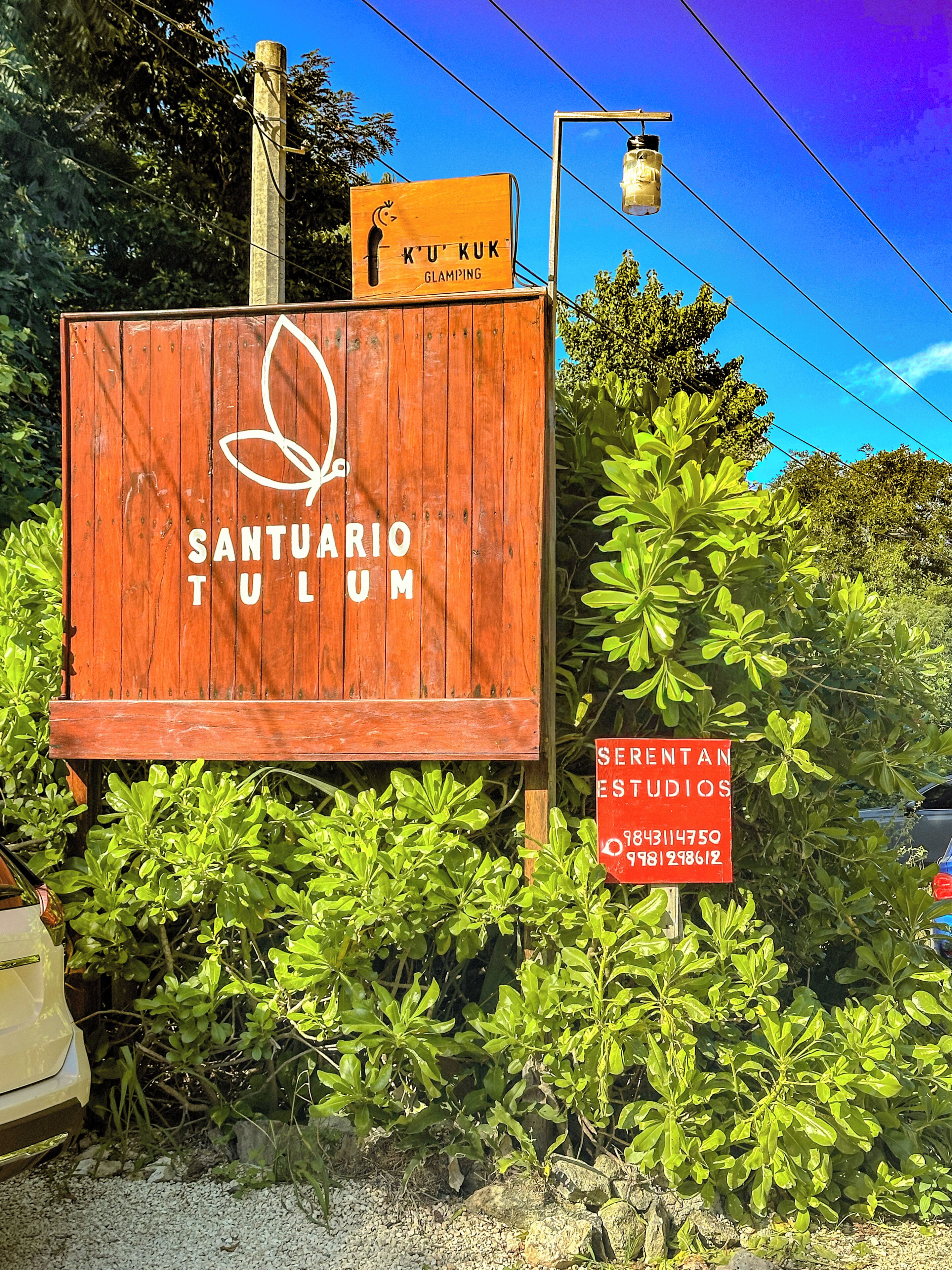 A wooden sign with 'SANTUARIO TULUM' and a logo, surrounded by greenery.