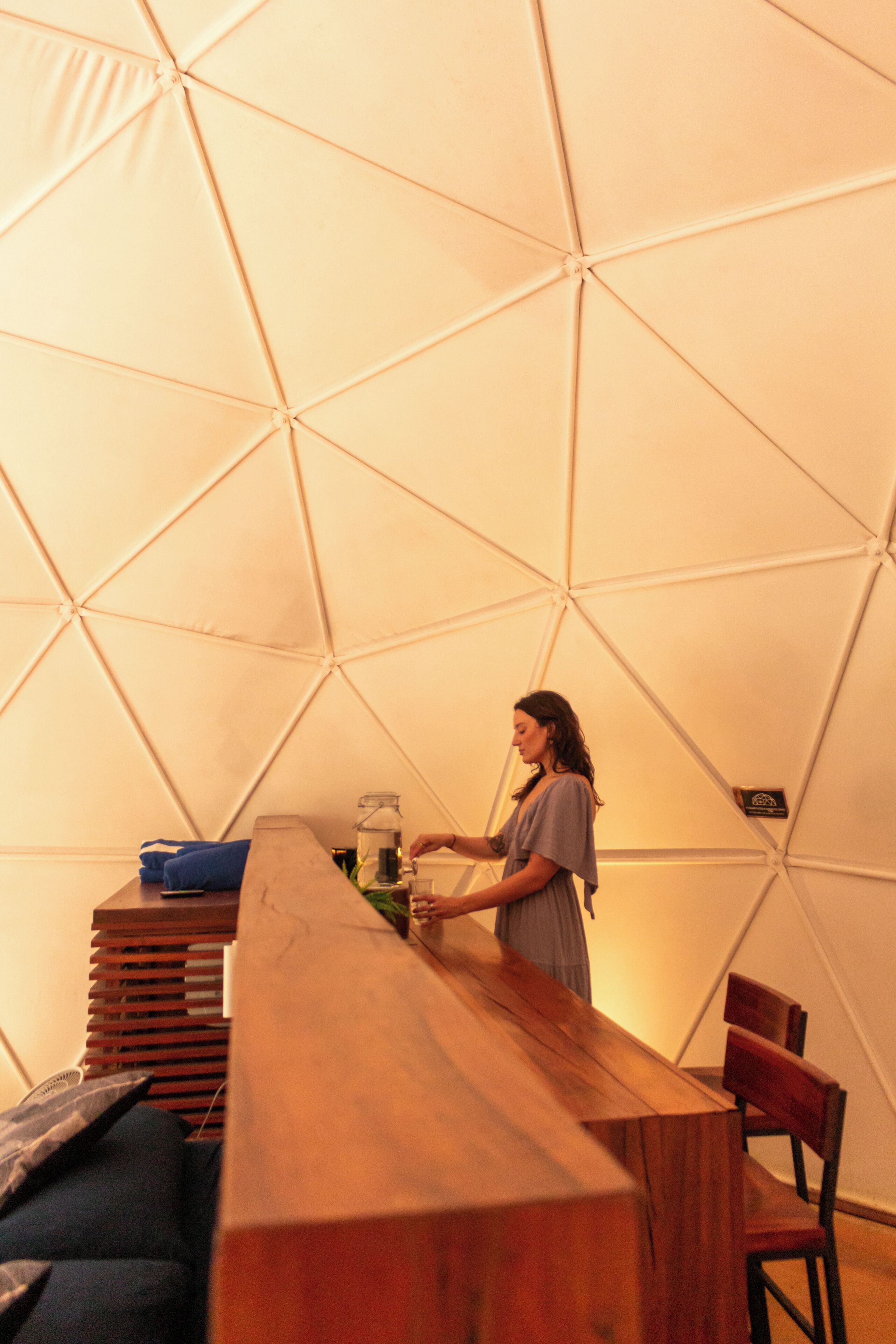 A tented accommodation with a wooden table and benches, a person at the table, and a geometric wall design.