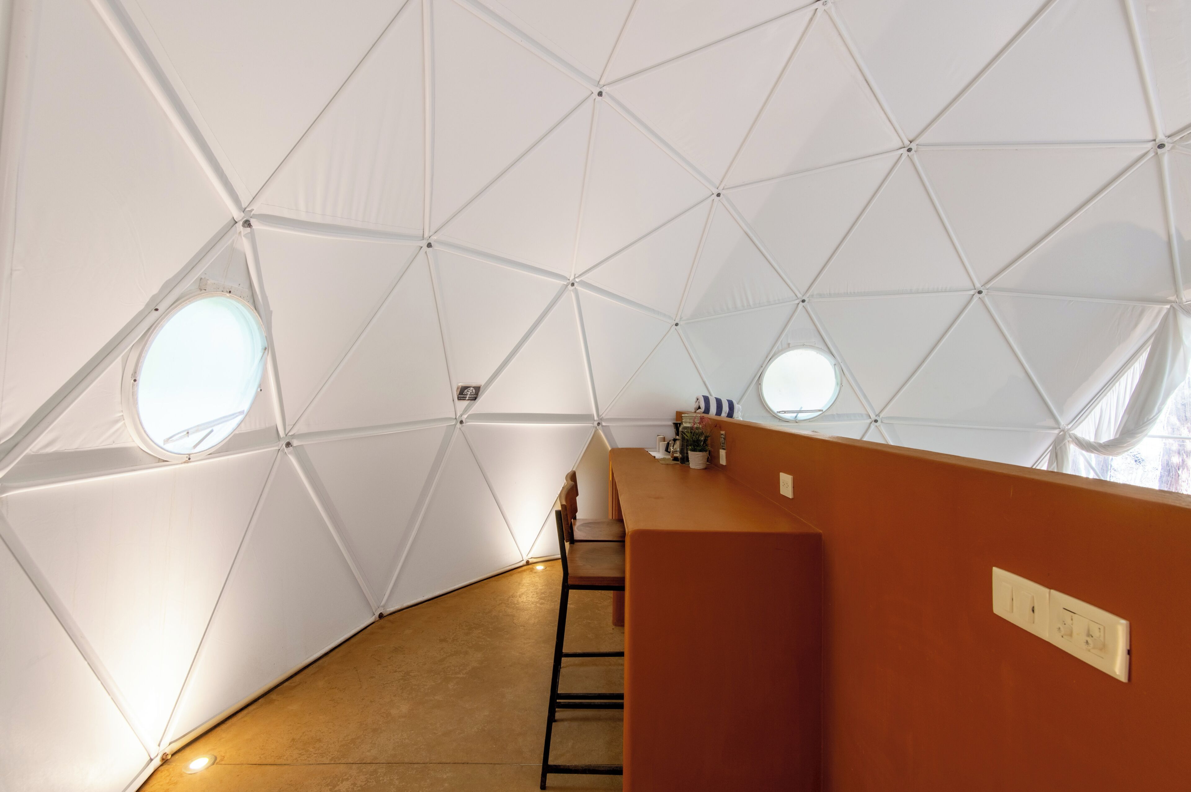 Interior de una cúpula geodésica con una mesa central, sillas y una pequeña zona de bar.