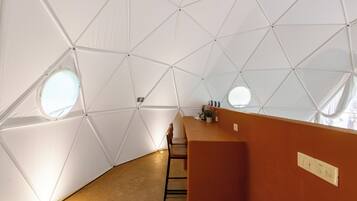 Interior de una cúpula geodésica con una mesa central, sillas y una pequeña zona de bar.