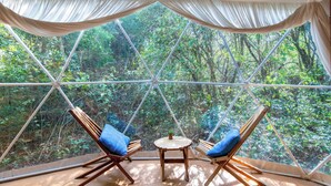 A geodesic dome with two wooden chairs and a small table, surrounded by a forest view.