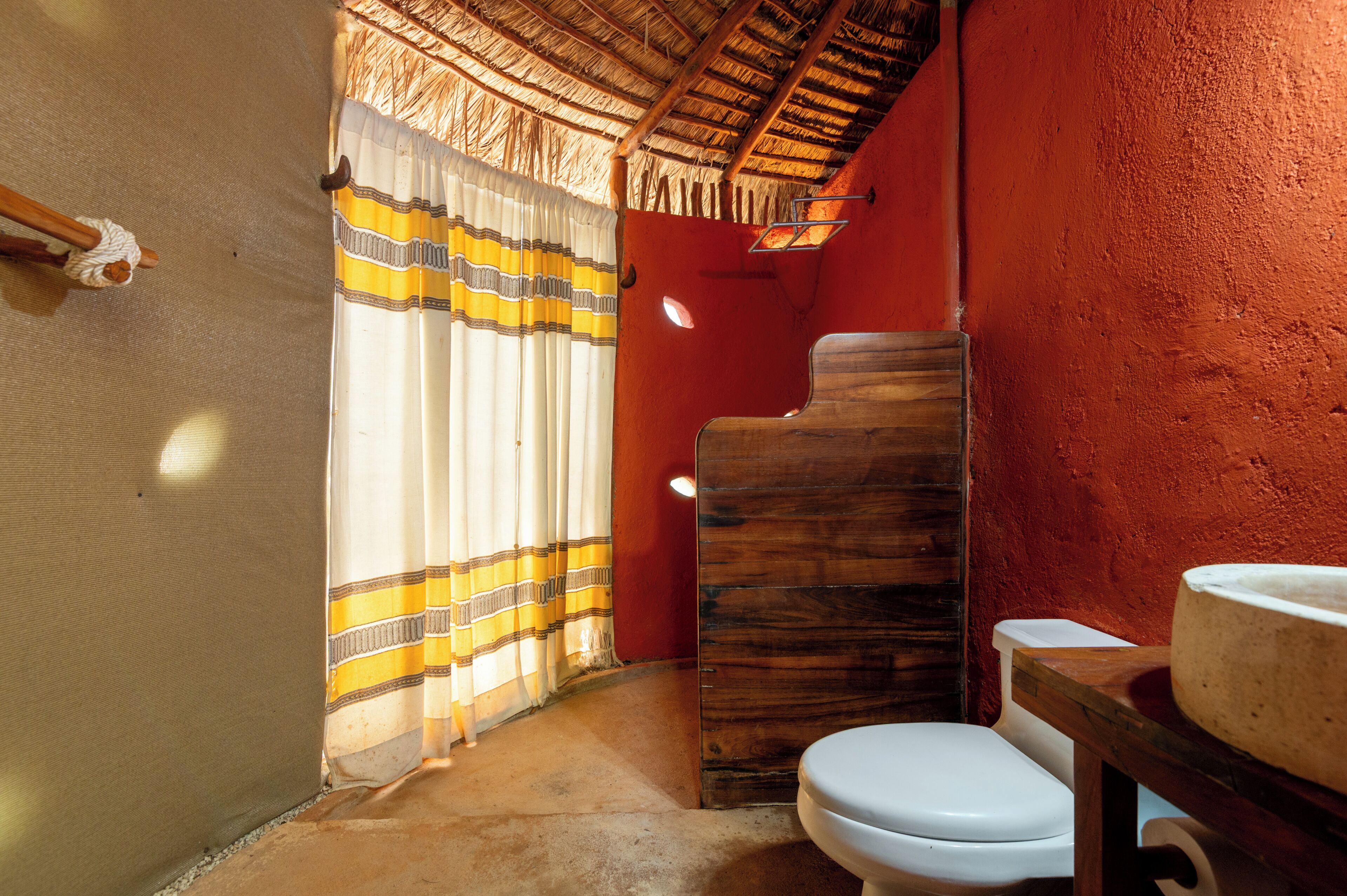Un baño con tocador de madera, inodoro blanco y cortina a rayas.