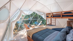 A tented accommodation with a bed, seating area, and view of greenery.