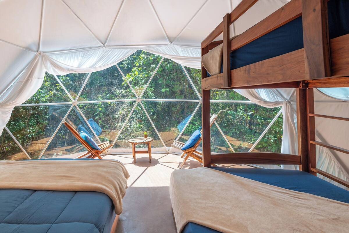 Een tentaccommodatie met twee bedden, een tafeltje en stoelen, met uitzicht op het bos.