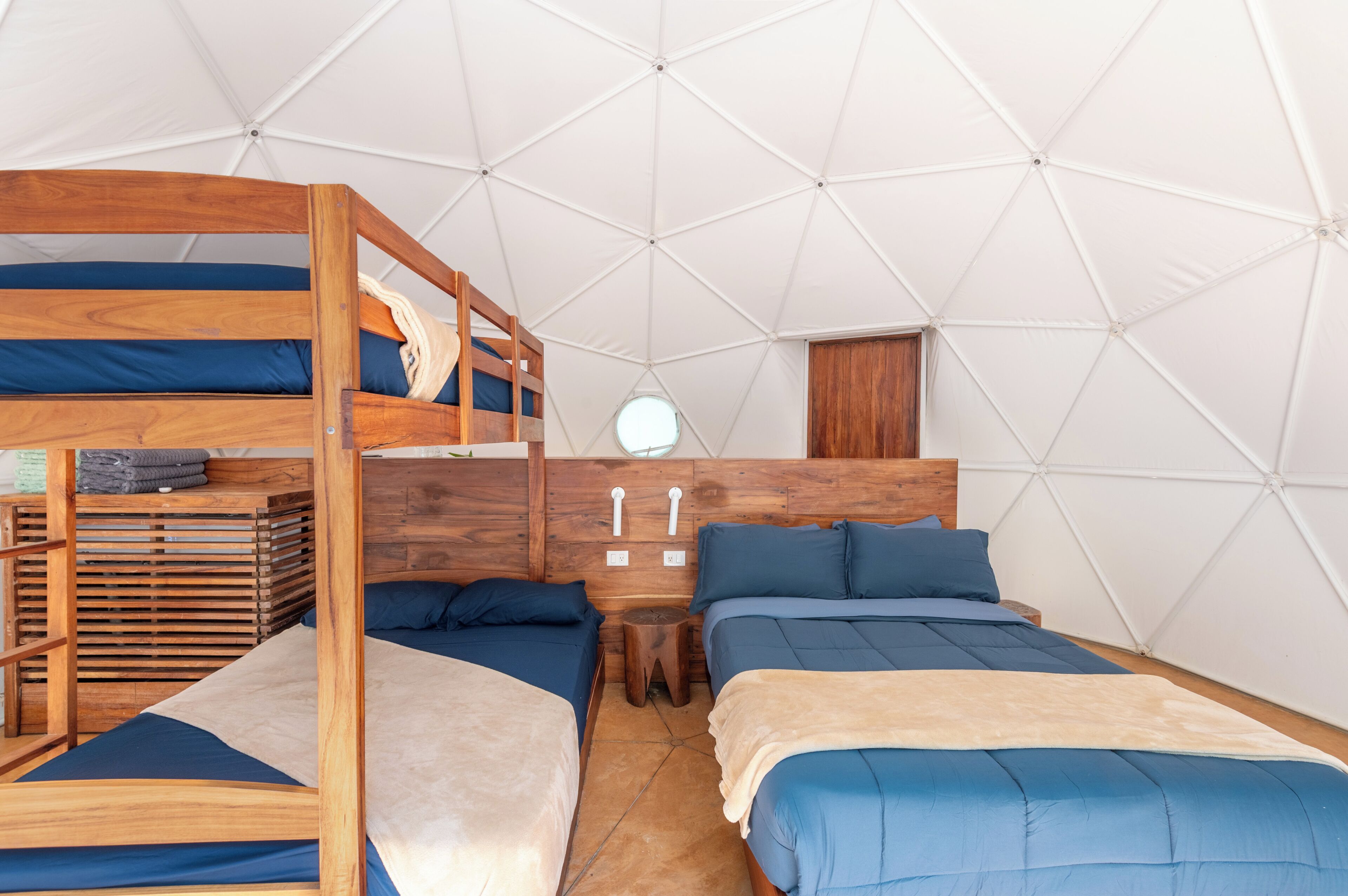A room with bunk beds, a wooden headboard, a small wooden stool, and a round window.