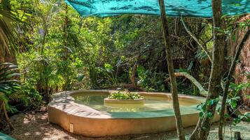 A circular hot tub surrounded by trees and a green canopy.