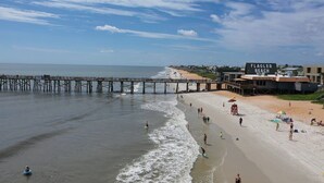 A beach with a pier extending into the water, a lifeguard tower, and a building labeled 'FLATLER BEACH'. - Heart of Flagler Beach-1 Blk 2 Beach-Pets Permitted-Walk EVERYWHERE! (Flagler Beach)