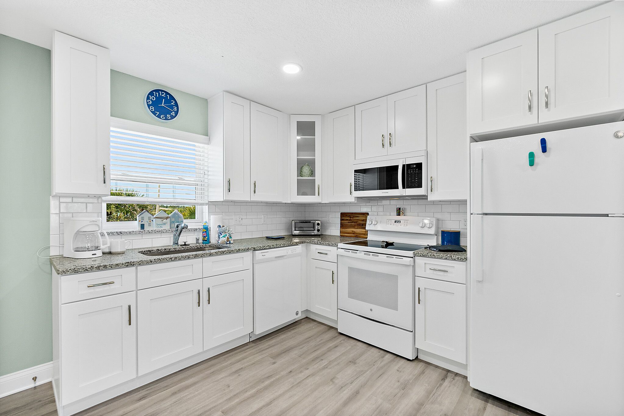 A modern kitchen with white cabinets, a microwave, an oven, and a refrigerator.