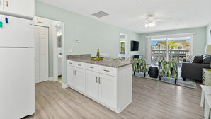 A modern kitchen with white cabinets, a granite countertop, and a built-in island. There is a dining area with a gray sofa and a view of the outside. - Heart of Flagler Beach-1 Blk 2 Beach-Pets Permitted-Walk EVERYWHERE! (Flagler Beach)