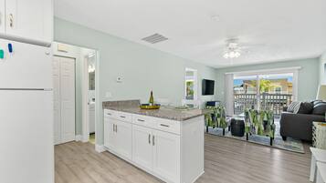 A modern kitchen with white cabinets, a granite countertop, and a built-in island. There is a dining area with a gray sofa and a view of the outside.