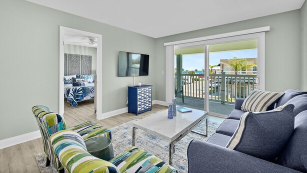 A living room with a sofa, armchairs, a coffee table, and a TV. There is a balcony with a view of the outside. - Heart of Flagler Beach-1 Blk 2 Beach-Pets Permitted-Walk EVERYWHERE! (Flagler Beach)