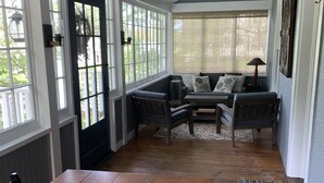 A cozy room with a wooden dining table set for four, a bench seating area, and large windows offering a view of the outdoors. - Walk into town, soak up sun on enclosed porch & steps away from nature trails! (Stockbridge)