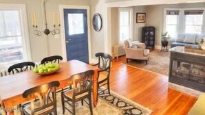 A dining area with a wooden table and chairs, a blue door, and a living room with a sofa and a fireplace. - Walk into town, soak up sun on enclosed porch & steps away from nature trails! (Stockbridge)