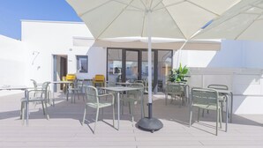 An outdoor patio area with tables and chairs, a large umbrella, and a building in the background. - Soho Boutique Columela (Cádiz)