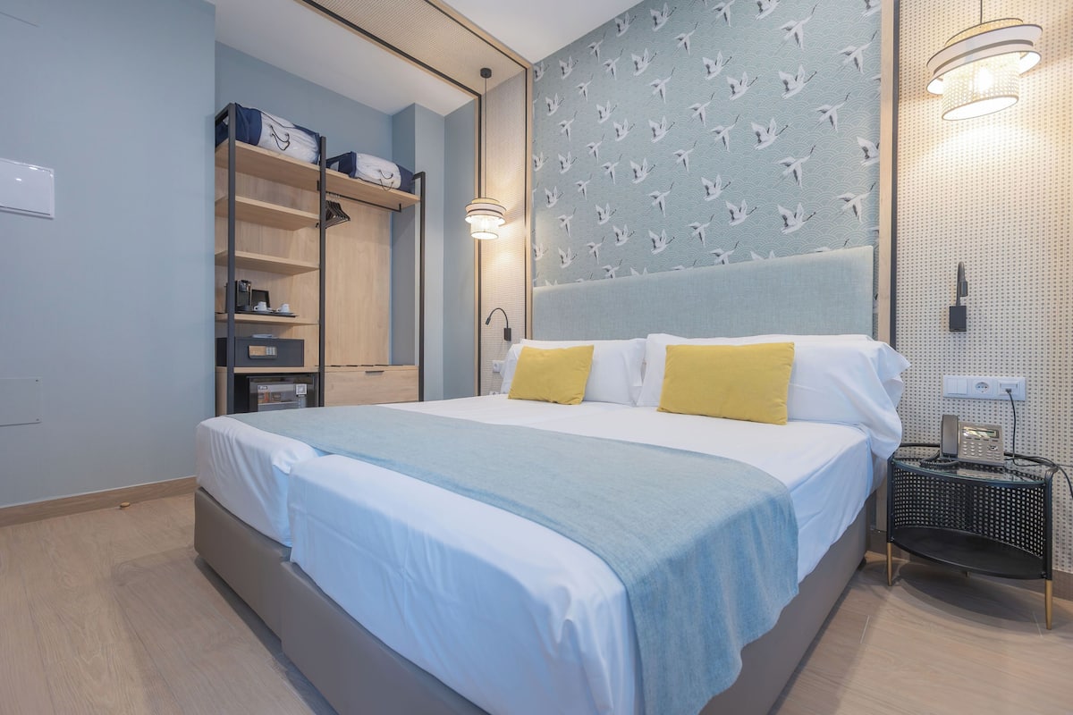 A modern hotel room with a large bed, a wardrobe, a bedside table, and a wall with a bird pattern.