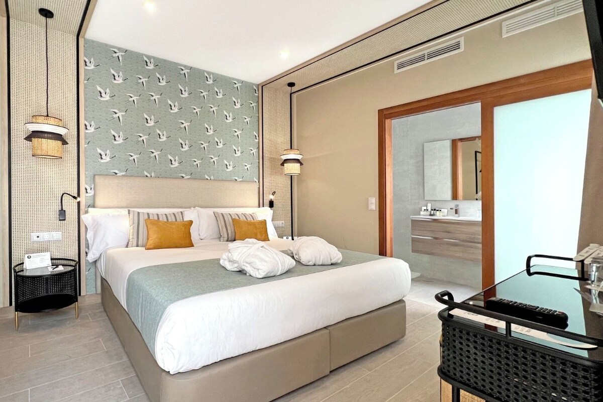 A modern hotel room with a large bed, a bedside table, a mirror, and a view of the bathroom.