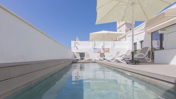 A swimming pool with lounge chairs and umbrellas, surrounded by white buildings. - Soho Boutique Columela (Cádiz)
