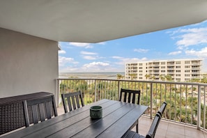 A balcony with a table and chairs, overlooking a beach and a building.