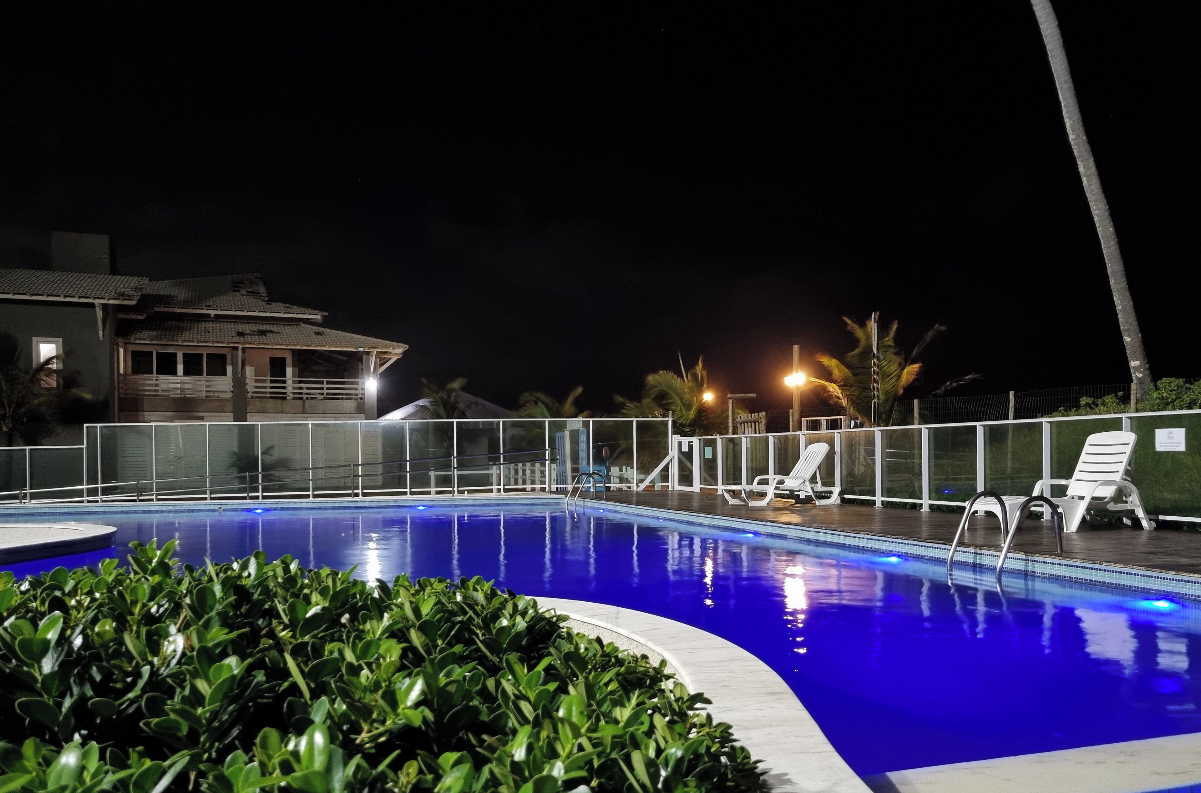 A swimming pool with a curved edge, surrounded by a fence and a few lounge chairs.