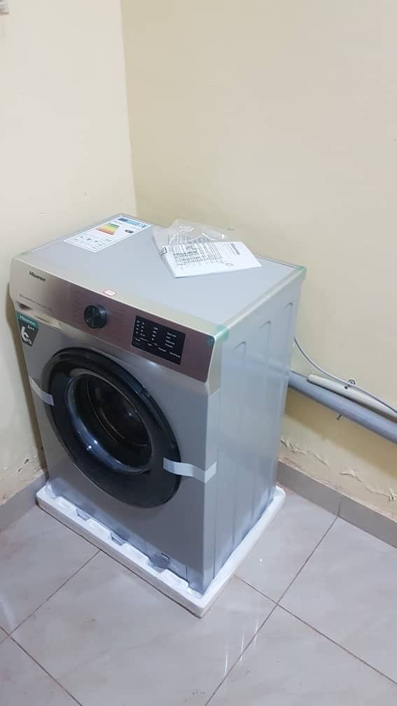 Un lave-linge compact et moderne, placé dans un coin d’une pièce dont le sol est carrelé et dont un des murs est uni.