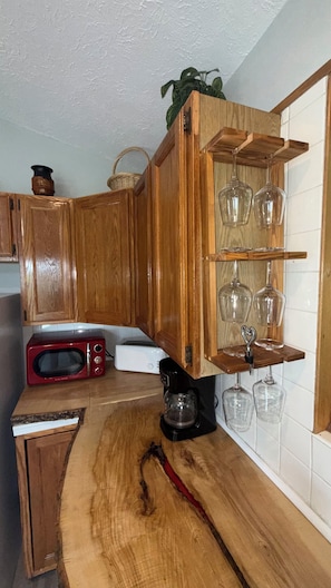 Eine Küche mit Holzausstattung, einer Mikrowelle, einer Kaffeemaschine und Weingläsern auf einem Regal.