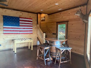 Un intérieur en bois agrémenté d’un baby-foot, d’une table ronde avec des chaises et d’une tête de cerf accrochée au mur.