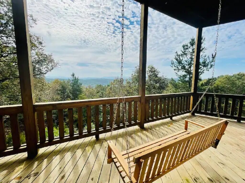 Eine Holzterrasse mit einer Schaukel und einer Bank, mit Blick auf eine bewaldete Landschaft.