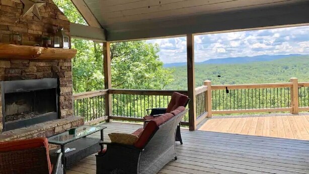 A covered outdoor area with a stone fireplace, wicker furniture, and a wooden deck overlooking a mountainous landscape. - Breathtaking LongRange Mntn Views 10min downtown BR & McCaysville Riverwalk (Blue ridge)
