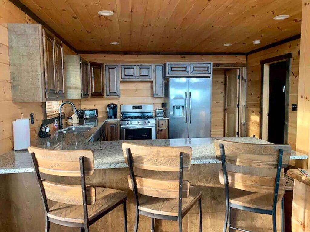 Een keuken met houten kastjes, een roestvrijstalen koelkast, een fornuis en een bar met houten stoelen.