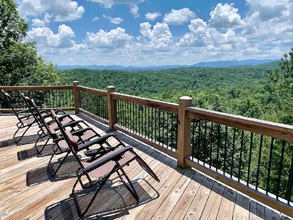 Une terrasse en bois avec des sièges extérieurs et une rambarde donnant sur un paysage boisé.