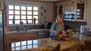A kitchen with a large island, wooden cabinets, and a window with blinds.