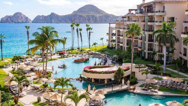 A resort with a central pool, multiple balconies, and a view of the sea.